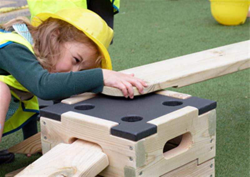 Child using Play Builder products to slot together a wooden plank into a wooden block